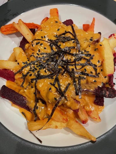 A red-orange cheese sauce on root veggie fries, garnished with sesame seeds and seaweed